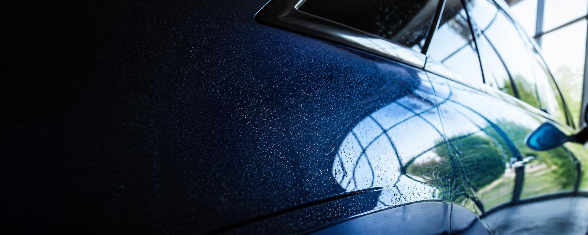 Close-up of a flawless mirror-finish car body panel with water beads after a professional detail